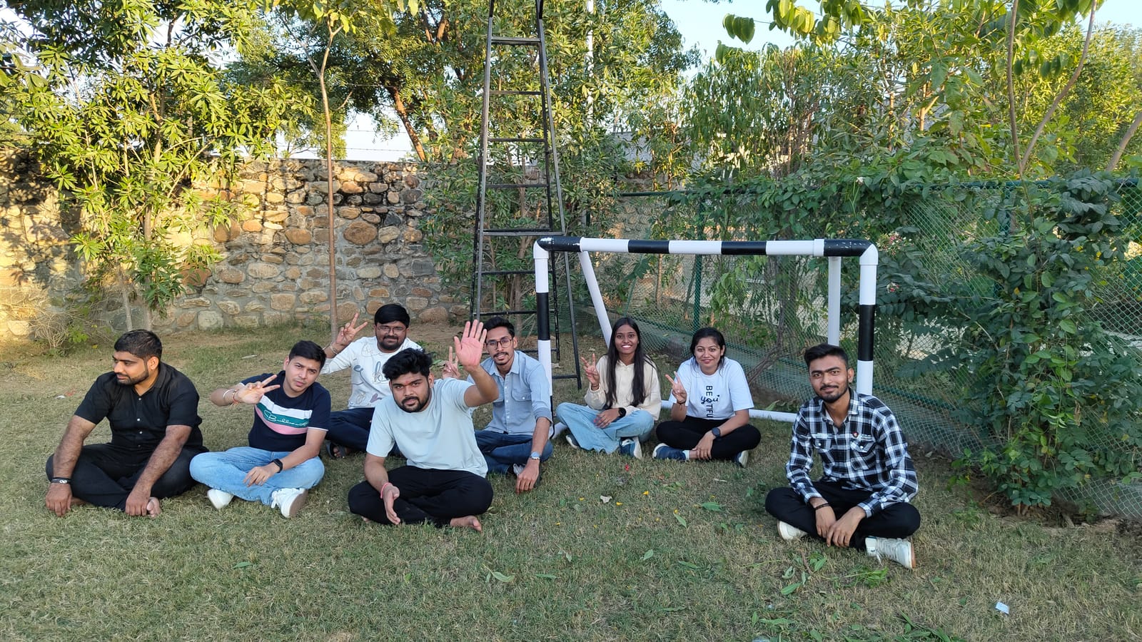 Team members sitting on the grass and waving at the camera
